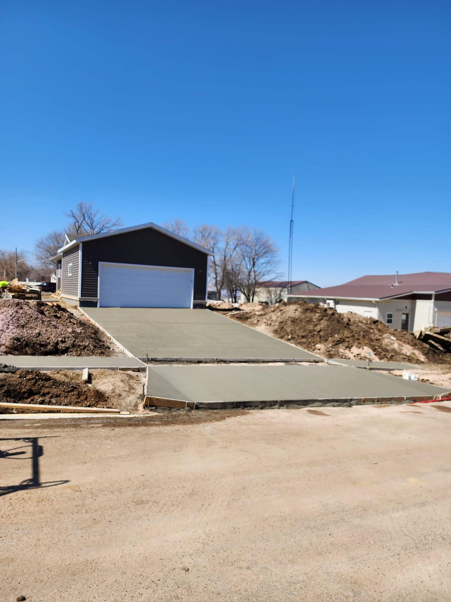 A fresh concrete driveway approach rising to a dark-sided outbuilding with a white overhead door under a clear blue sky