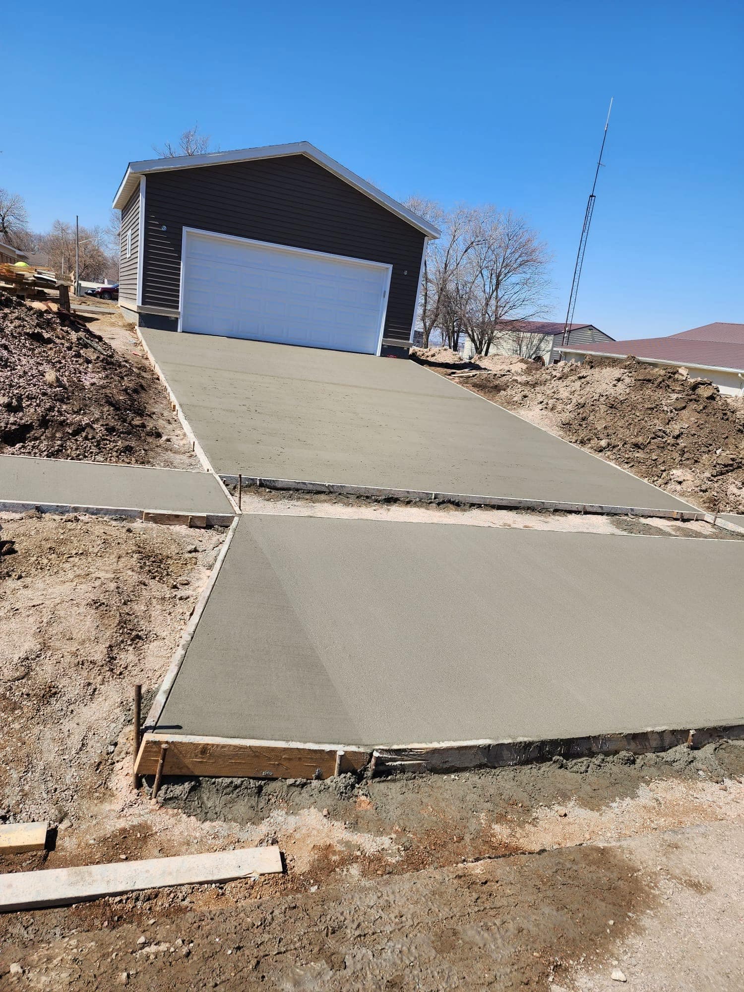 A fresh concrete driveway sloping up to a dark-sided outbuilding with a white overhead door, forms still along its edges