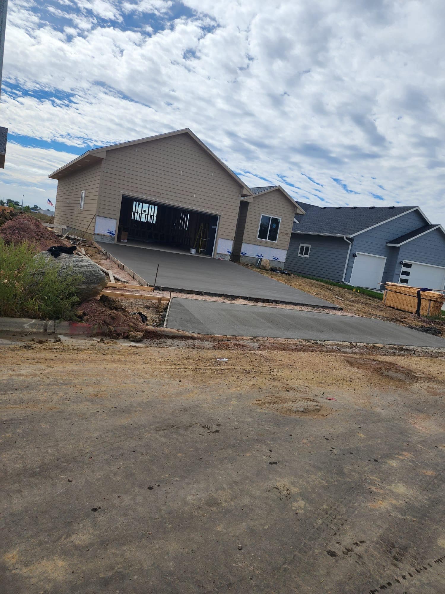 A fresh concrete driveway sloping to the street from the open framed garage of a new home