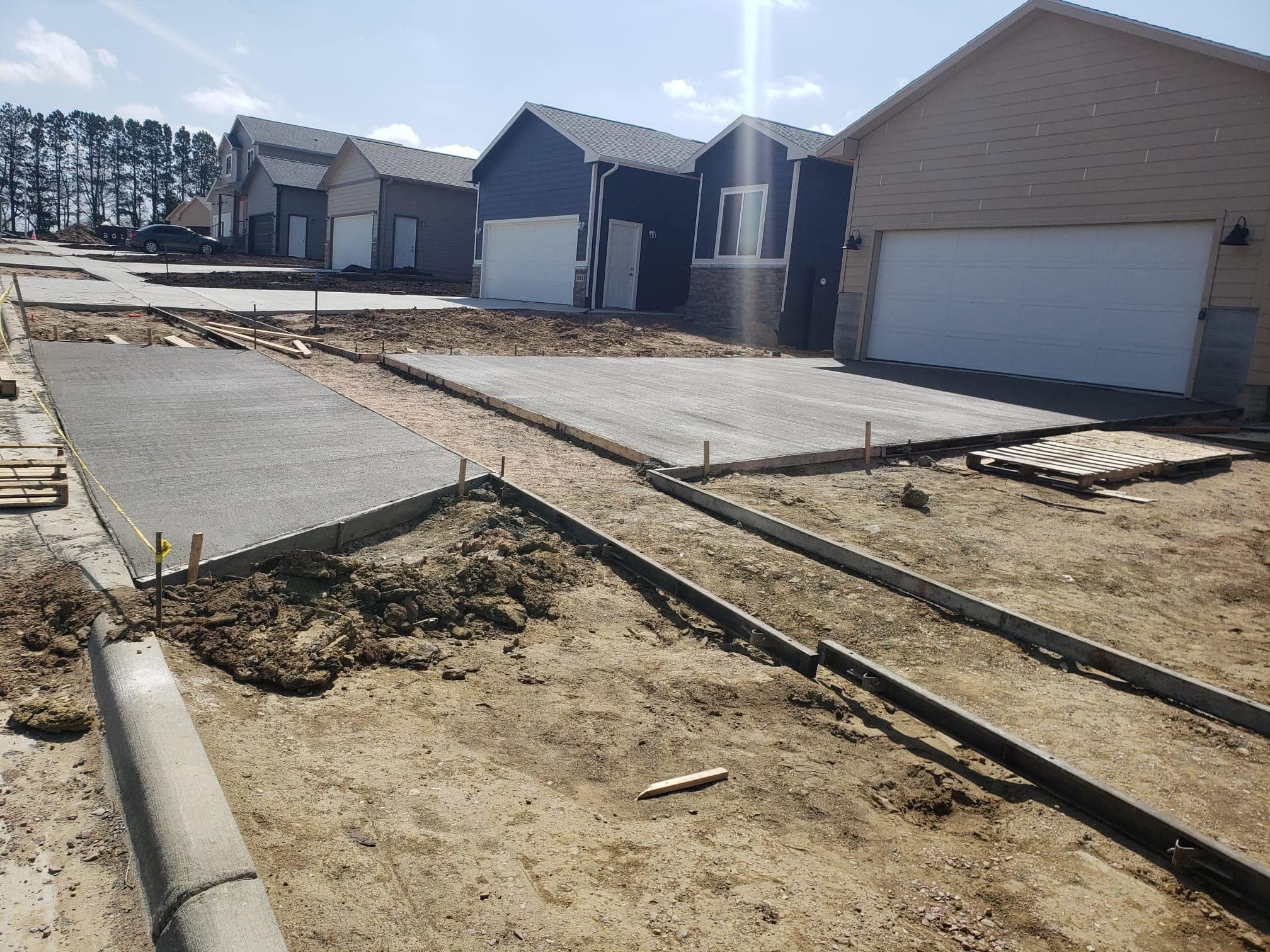 A fresh broom-finished concrete driveway and sidewalk, forms still in place, in front of a row of new homes with attached garages