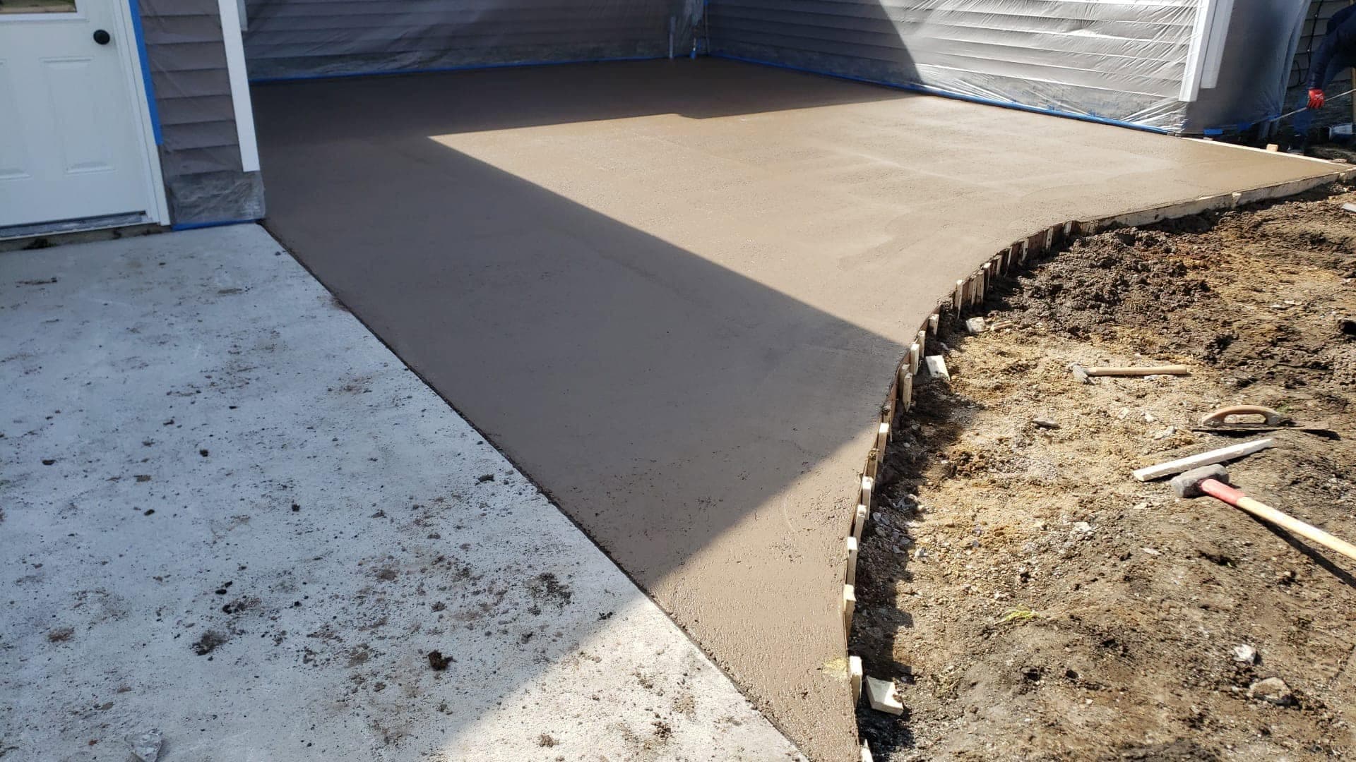 A fresh troweled concrete patio with a curved formed edge, poured against a house wrapped in protective plastic sheeting