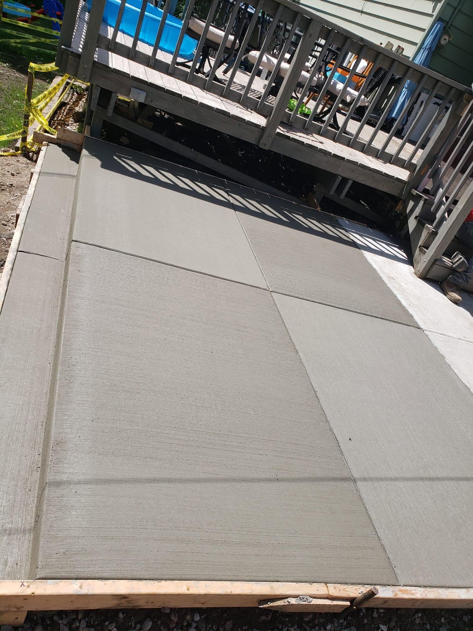 A fresh broom-finished concrete patio landing at the base of a deck near an above-ground pool