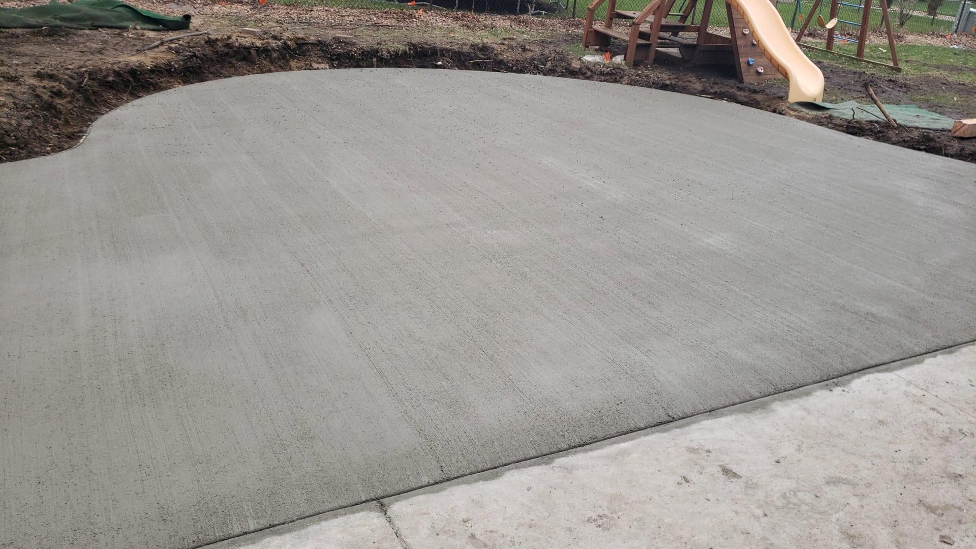 A finished curved backyard concrete patio with a formed edge, poured over a compacted base
