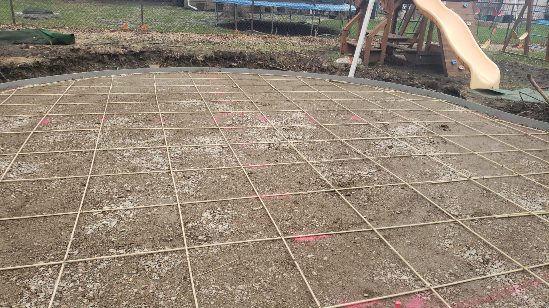 A steel reinforcing mesh grid laid over the graded base of a curved backyard patio before the pour