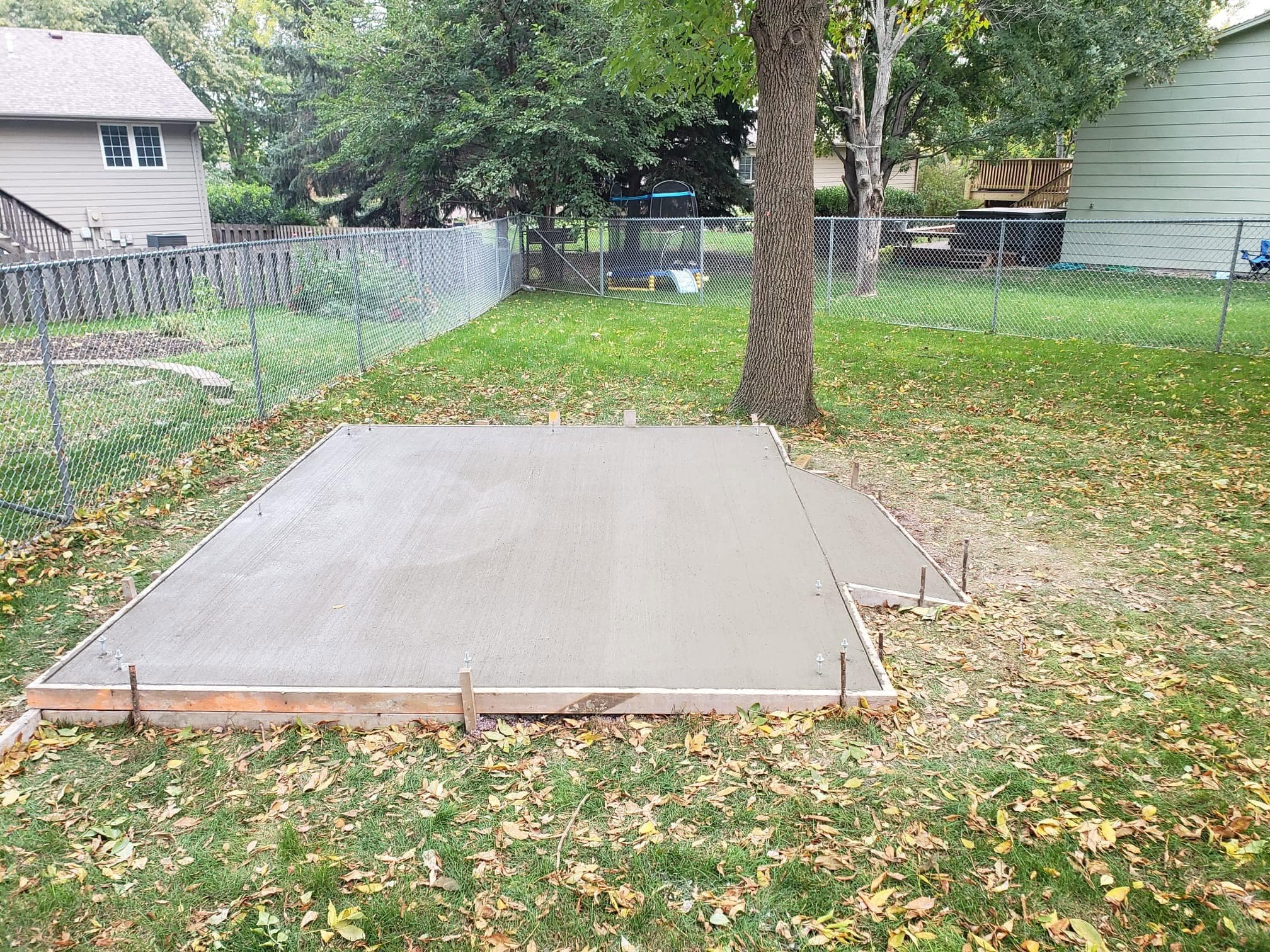 The same fenced backyard with the fresh concrete slab poured inside its forms