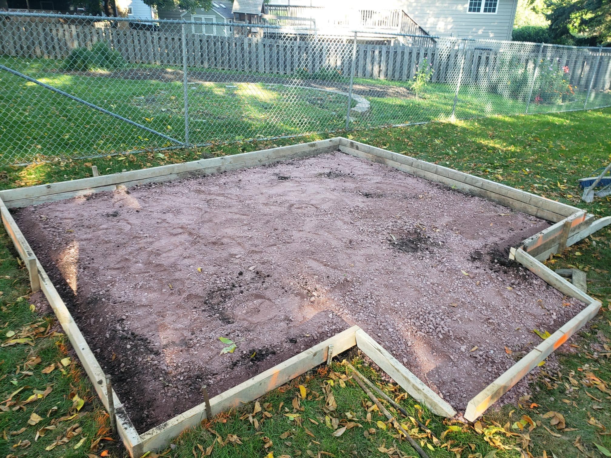 Wood forms set around a compacted gravel base pad in a fenced backyard, before the pour