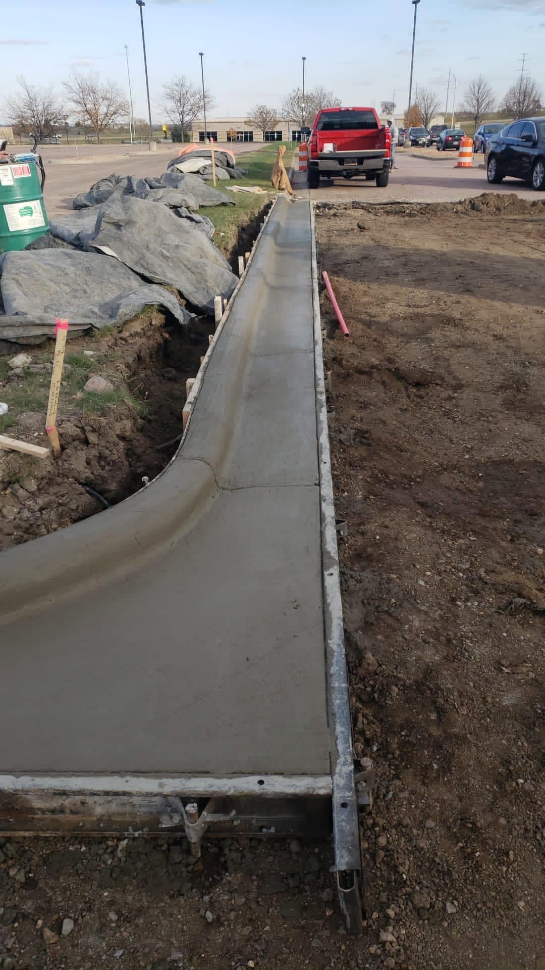 A freshly poured curved concrete curb and gutter run along the edge of a commercial parking lot