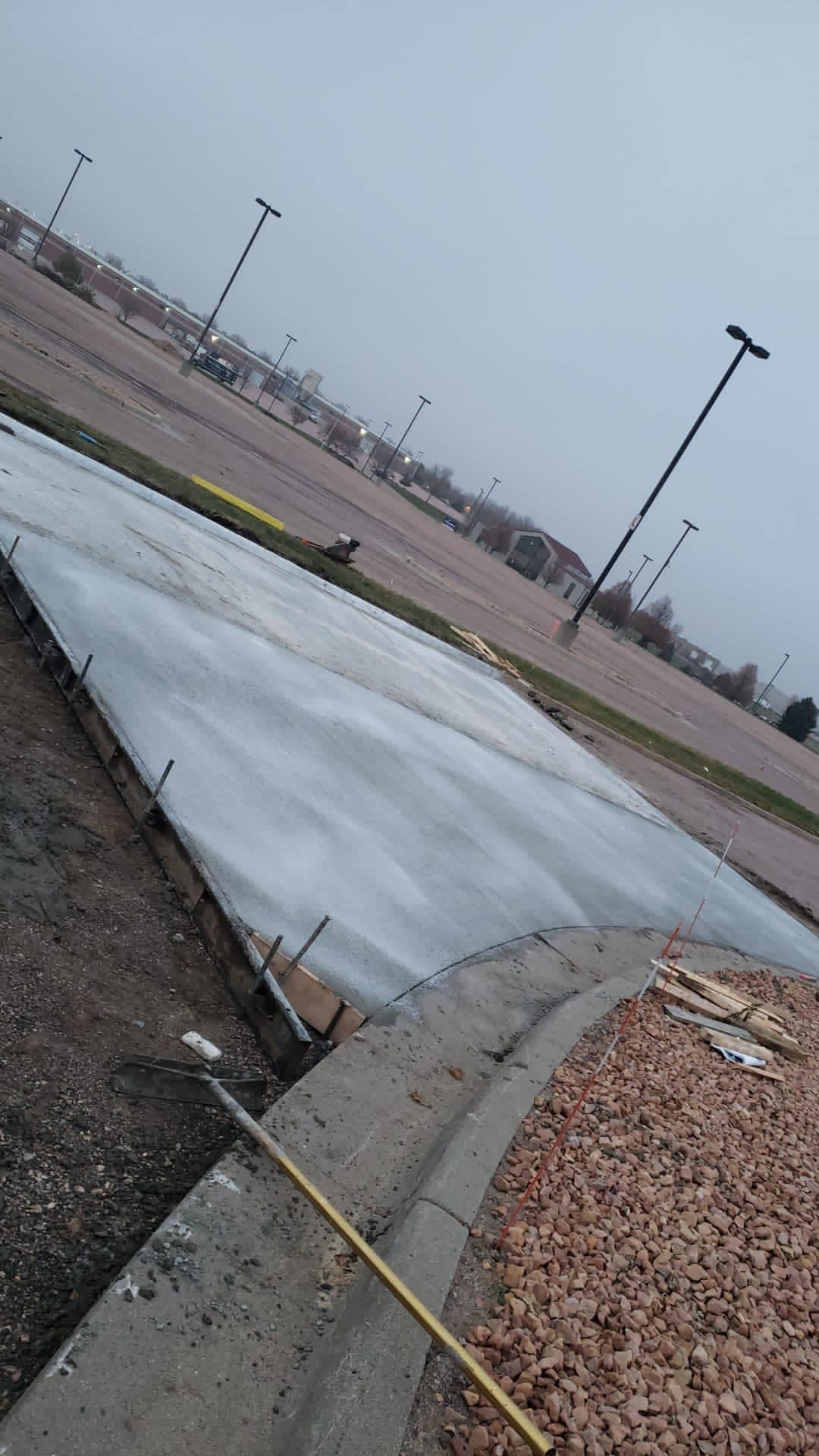 A fresh concrete slab covered with plastic sheeting to cure, steel stakes along its formed edge