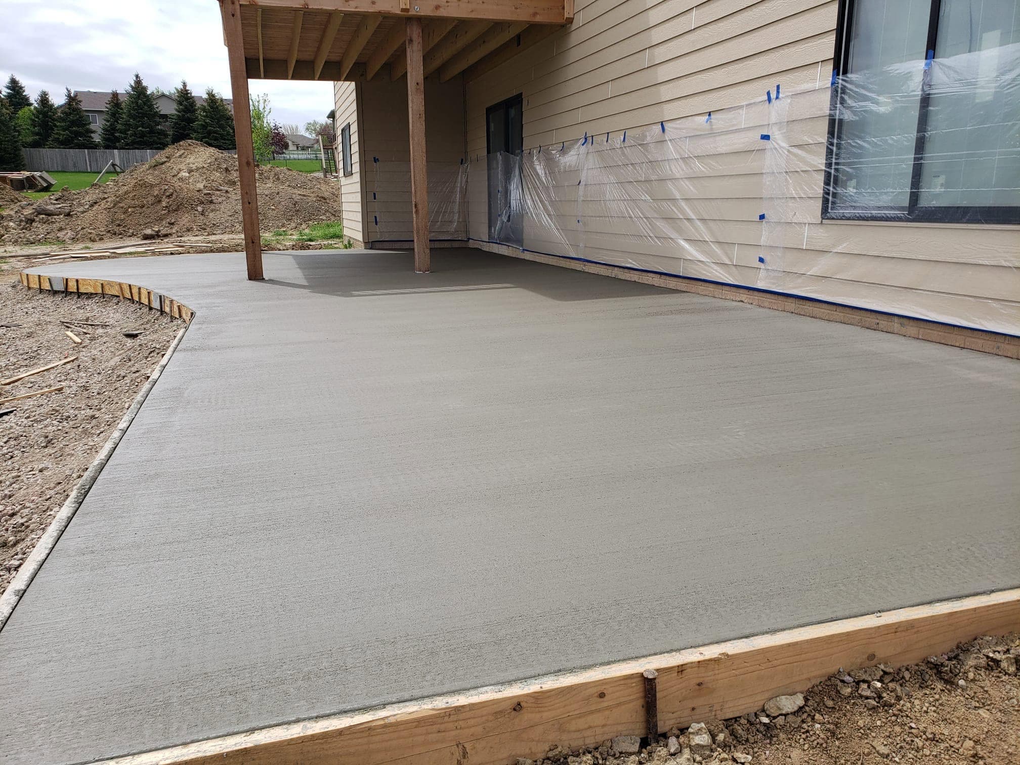 A large fresh finished concrete patio poured under the covered deck of a home