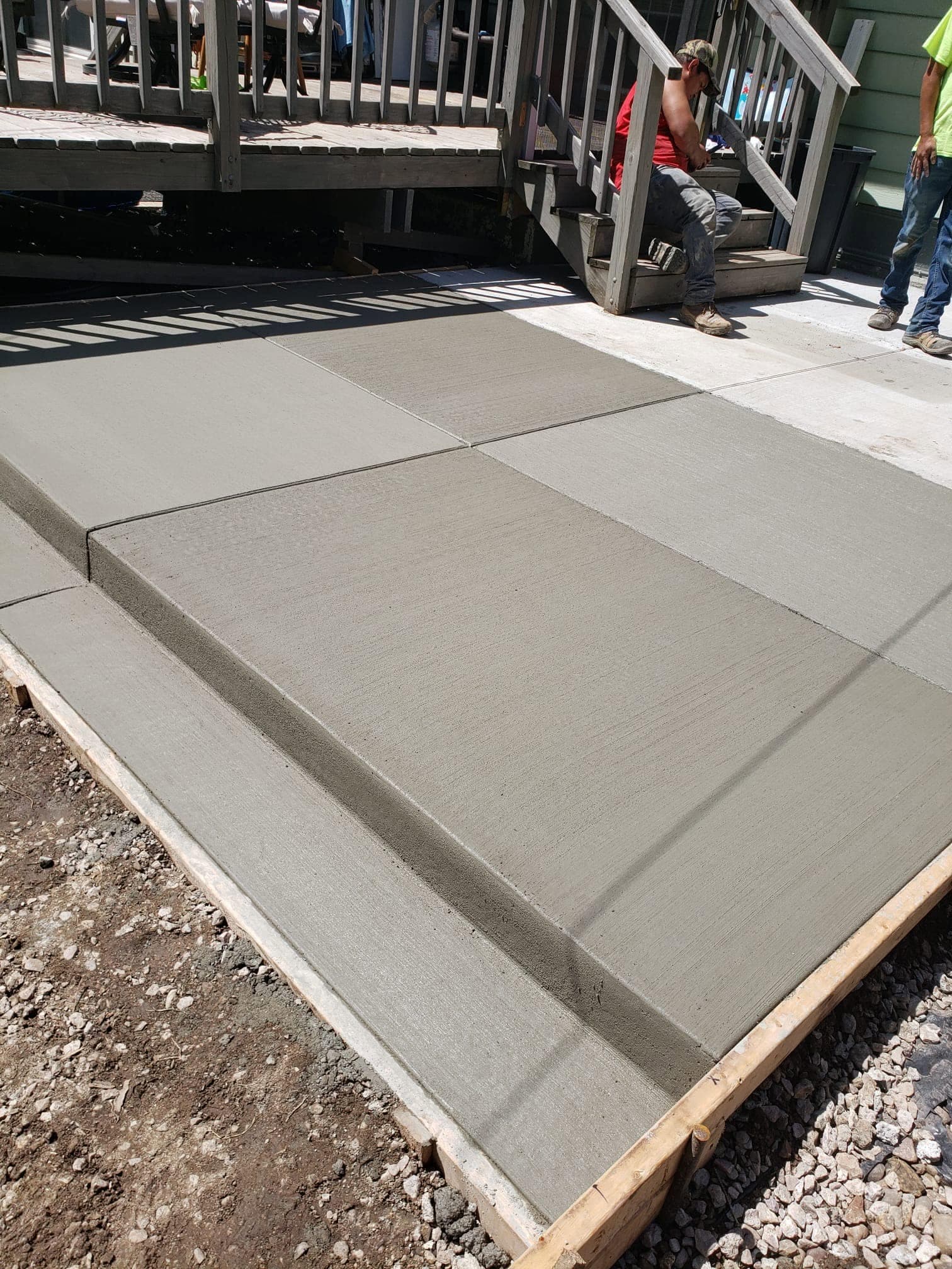 A fresh broom-finished concrete landing at the base of a wooden deck stairway