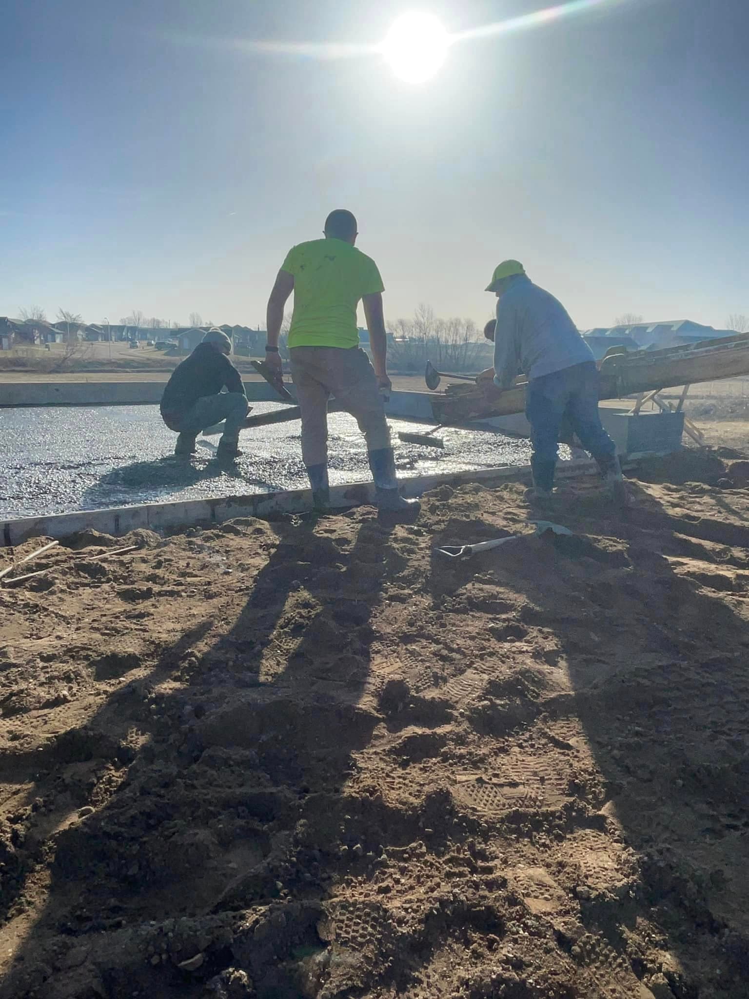 The crew spreading and striking off wet concrete across a fresh slab in the sun