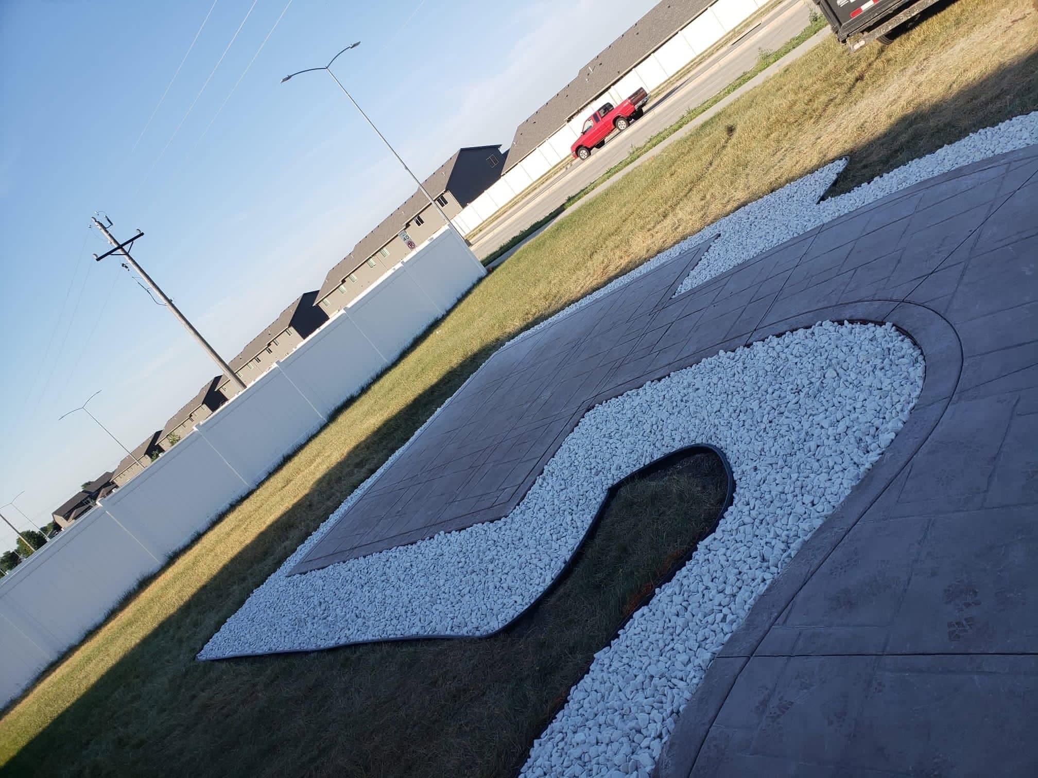 A stamped and colored concrete patio with a curved bed of white decorative rock set into it
