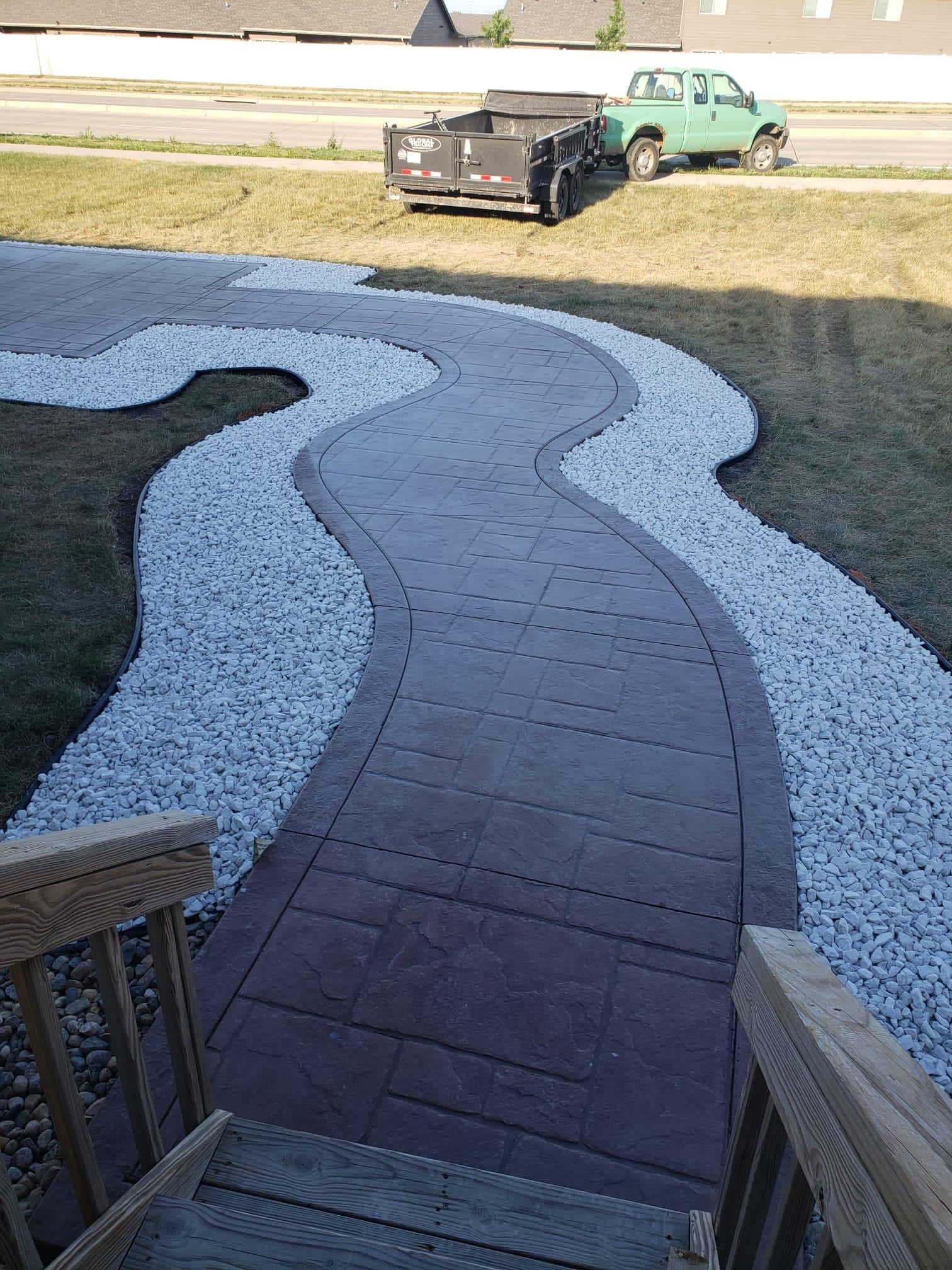 A stamped and colored concrete walkway winding through a bed of white decorative rock