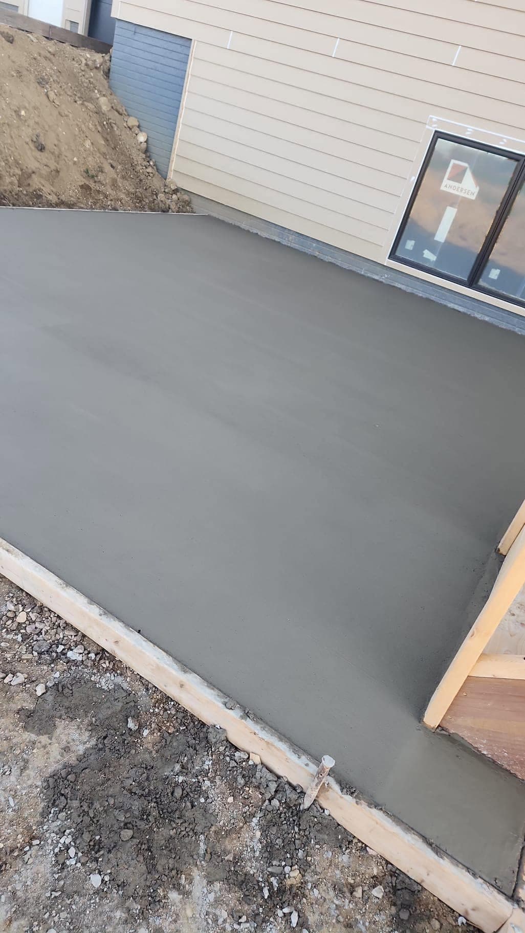 A fresh finished concrete walkway curving alongside a house with a formed edge