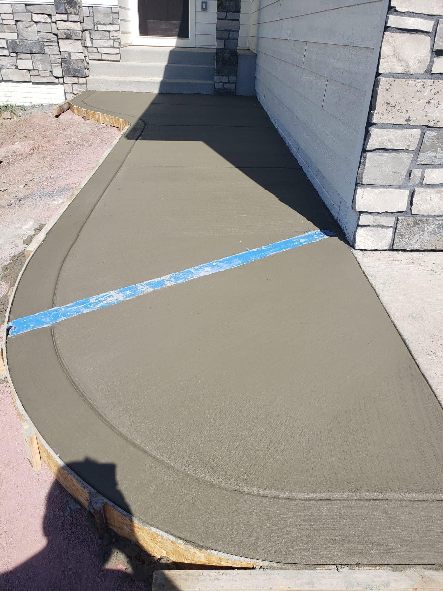 A finished concrete walkway curving around the stone-column front entry of a home